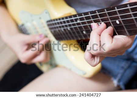 female teen musician, guitarist fingers playing on electric guitar / focus to left hand on rosewood fingerboard