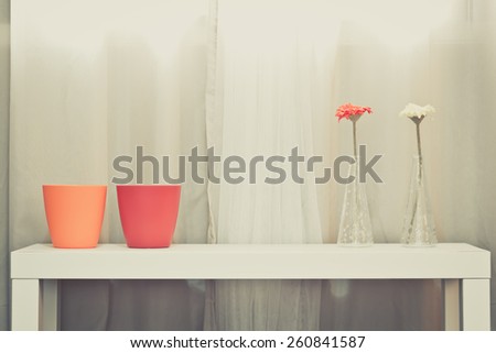 red, orange pots & red, yellow flowers in glass vase on white table on soft color curtain background + art filter