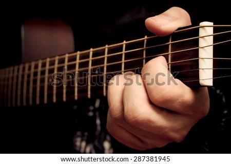 left hand of musician, guitarist playing D chord on acoustic guitar fingerboard for music background