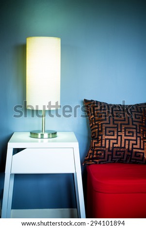 Lamp on white table next to red seat & pillow in living room at night for interior background