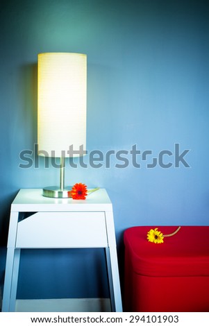 Lamp on white table next to red seat & flowers in living room at night for interior background