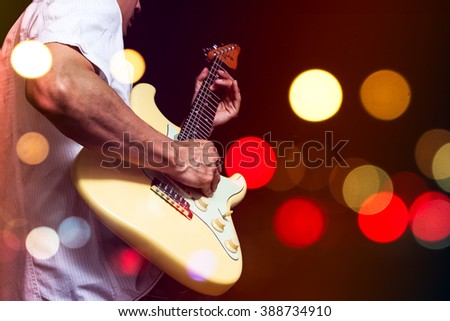 asian musician playing electric guitar with colourful bokeh light on stage