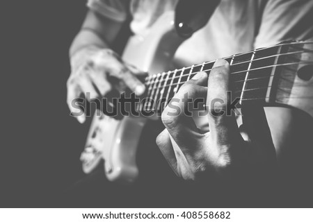 closeup male guitarist hands playing electric guitar on stage + bw film filter for music background