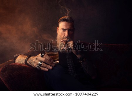 Portrait of an attractive business man with a cigar and a glass of whiskey in a dark room