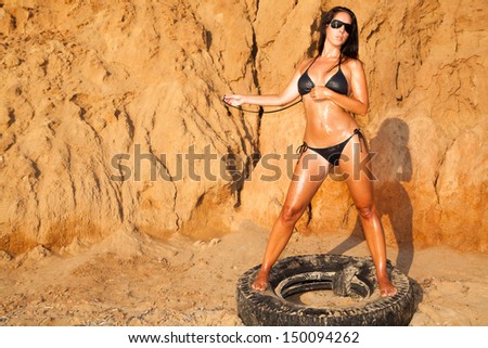Lubricated woman in bikini with car tires on the beach