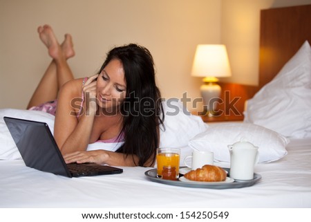 Beautiful girl with a laptop is having breakfast in a hotel bed