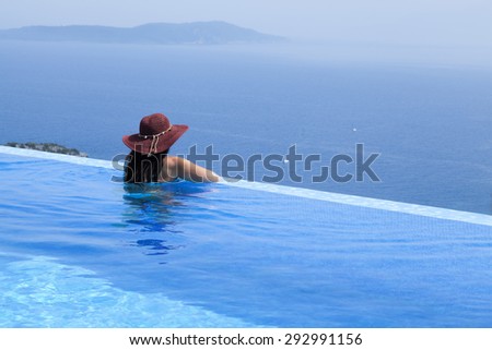 Beautiful woman with a hat is relaxing in an infinity pool with a breathtaking view