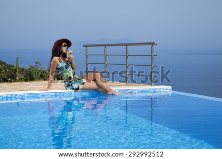 Beautiful woman in a sundress and a with cocktail is relaxing on an infinity pool