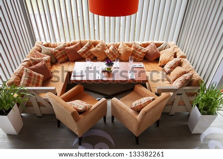 Interior of modern restaurant with a big orange sofa two orange chairs, an orange lamp and the laid table.Top view