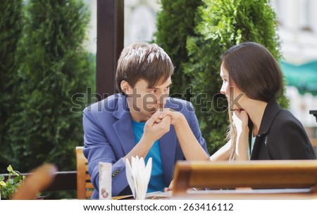 Man kissing a woman\'s hand at a summer cafe