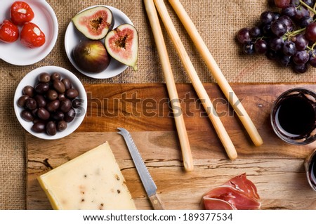 Italian Antipasto table setting with Pecorino Cheese, Wine, Figs, Grapes, Olives, Prosciutto, Stuffed Peppers, and bread sticks on chopping board.