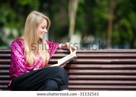 Attractive girl student reading book in summer park.
