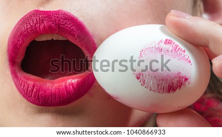 Easter egg concept. Lipstick print on round egg. Female mouth and red fashionable lipstick. Beautiful symbol of femininity life. Woman or girl holding an egg and kiss. Cosmetics for housewife. Food