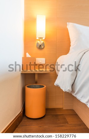 Lamp on a table next to a bed and switch,Box of tissues,Trashcan