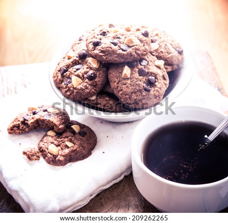 Chocolate chip cookies on napkin and hot tea on wooden table. Stacked chocolate chip cookies close up. split toning color image
