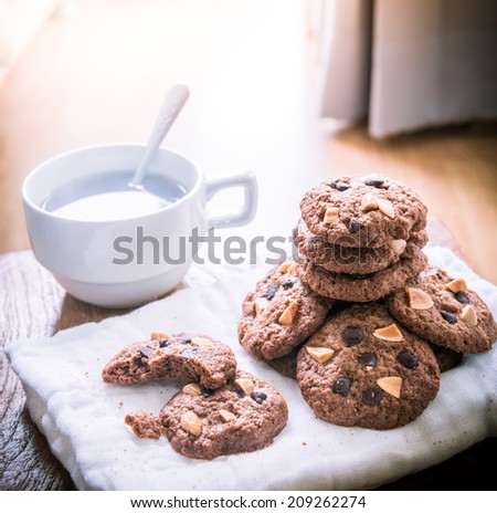 Chocolate chip cookies on napkin and hot tea on wooden table. Stacked chocolate chip cookies close up. split toning color image