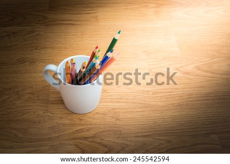 Color pencils in white coffee cup on wooden background