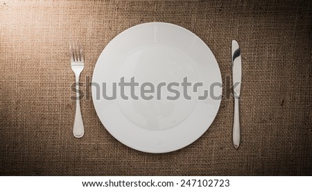 Empty white plate   fork, knife on sackcloth background