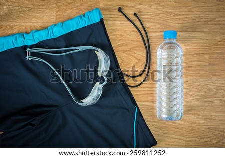 glass and Swimming trunks and water Bottles on wooden background