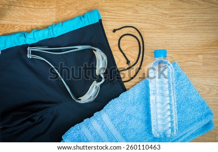 glass and Swimming trunks , water Bottles , towel on wooden background