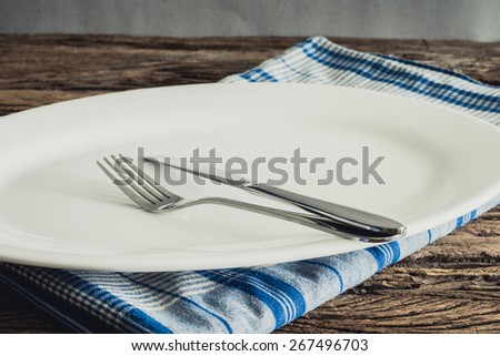 White Plate on a napkin and silver  fork , knife. on wooden tabletop against grunge wall. vintage tone