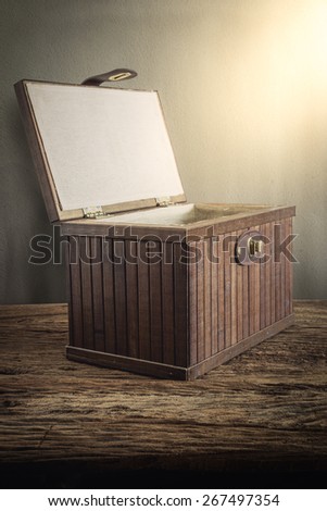 Old wooden chest with open lit on wooden tabletop against grunge wall. vintage tone