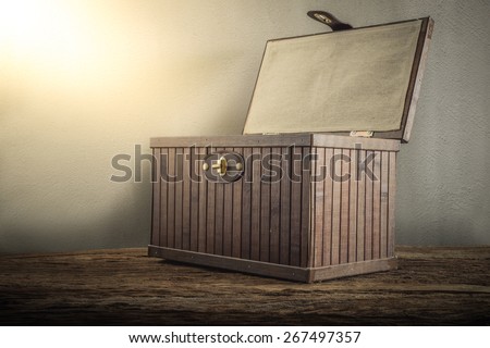 Old wooden chest with open lit on wooden tabletop against grunge wall. vintage tone