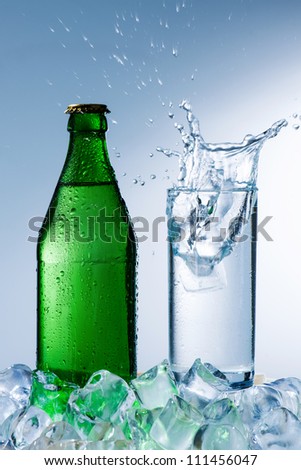 bottle of mineral water with ice and a glass with water splash on a blue background
