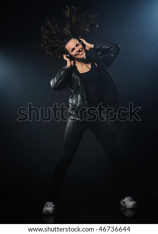 Young woman listening to music and dancing on a black background