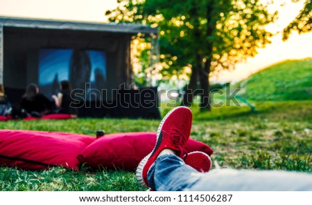 Red snickers shoes on ground and big movie screen in open cinema in green public park.Enjoying and relaxing on summer weekend.