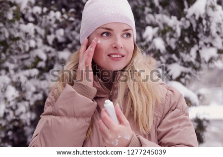 Woman applying skin cream on face and hands,protecting from cold weather on winter season.Blonde girl take care of skin outdoors on snowy nature