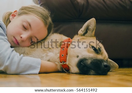 Little girl sleep embracing her dog on the parquet floor. Pet and child love.