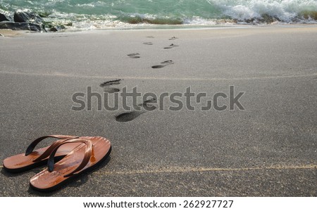 Human leave his flip flops on the black sandy beach and go to swim