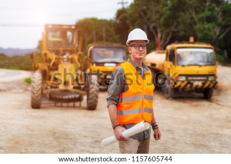 Handsome engineers wear protective helmets and are standing with road construction vehicles background.