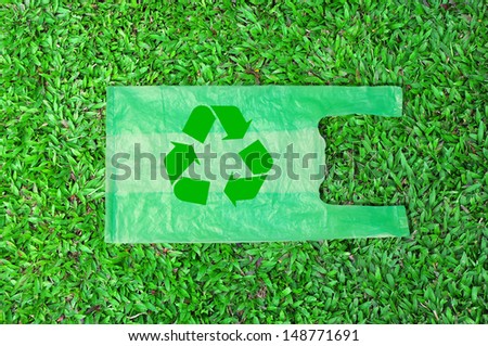 green plastic bag with recycle reduce reuse sign on green field