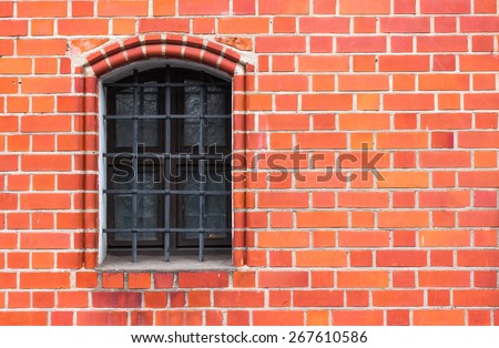 A fragment of a red brick house with the window, decorated with steel window grating