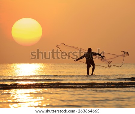 Silhouette asian fisherman throwing net in the sea at morning with big yellow sun. Hua Hin, Thailand