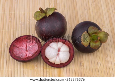 Mangosteen fruits on natural colour bamboo mat with one fruit cut open