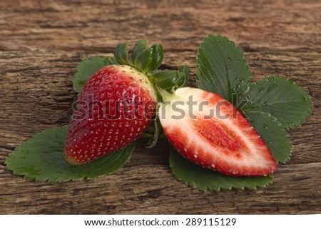 Fresh Strawberry one cut half place on strawberry leaves on old timber board blur background