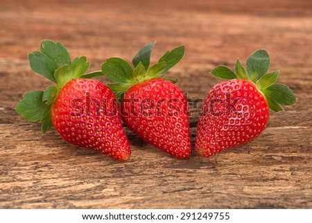 Three red ripe strawberries arranged on old rustic look timber with out of focus timber in the background