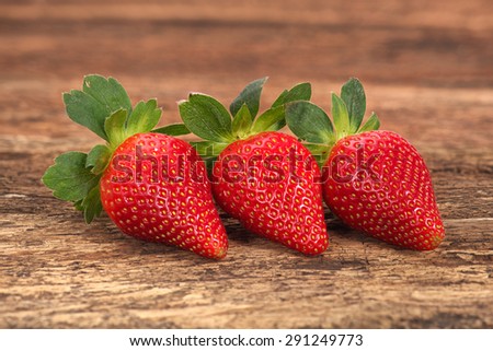 Three red ripe strawberries arranged formally on old rustic look timber with out of focus timber in the background