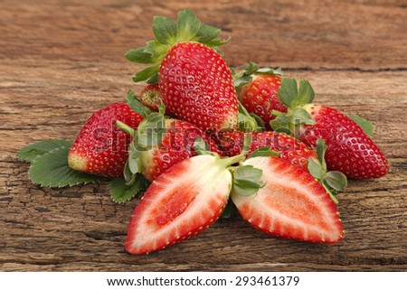 Fresh red ripe whole strawberries and leaves with one cut half on old rustic look timber