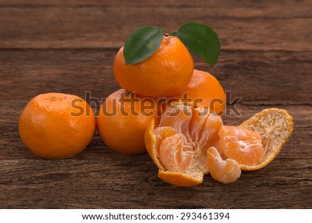 Ripe Mandarin fruit with leaves and one peeled open place on old rustic look timber