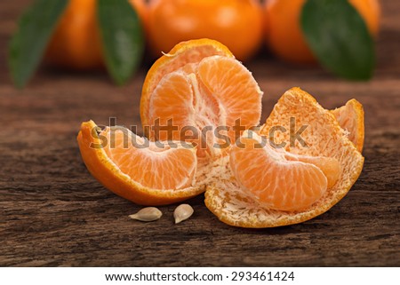 Ripe Mandarin fruit peeled open and place on old rustic look timber with group of mandarin fruits and leaves out of focus on the background