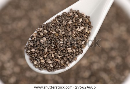 Dry chia seeds healthy super food in a white ceramic spoon lift above out of focus chia seeds in the background