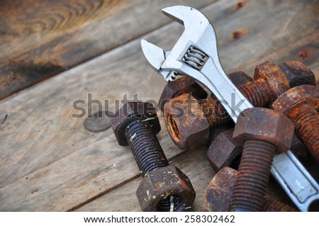Old bolts with adjustable wrench tools on wooden background.
