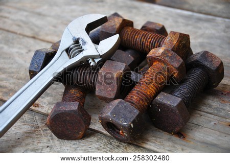 Old bolts with adjustable wrench tools on wooden background.