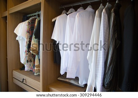 Clothes hang on a shelf in a designer clothes store, modern closet with row of cloths hanging in wardrobe, vintage rooms.