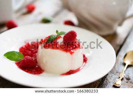 Delicious italian dessert panna cotta with raspberry sauce and mint in white plates on wooden background