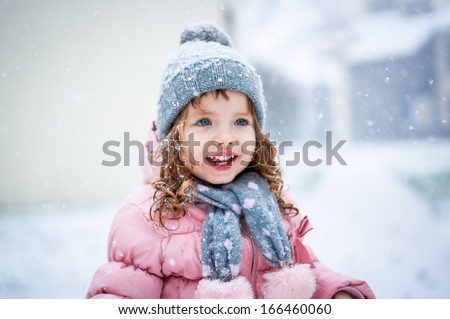 Cute Baby Girl In Pink Jacket And Grey Hat Enjoying First Snow Blowing